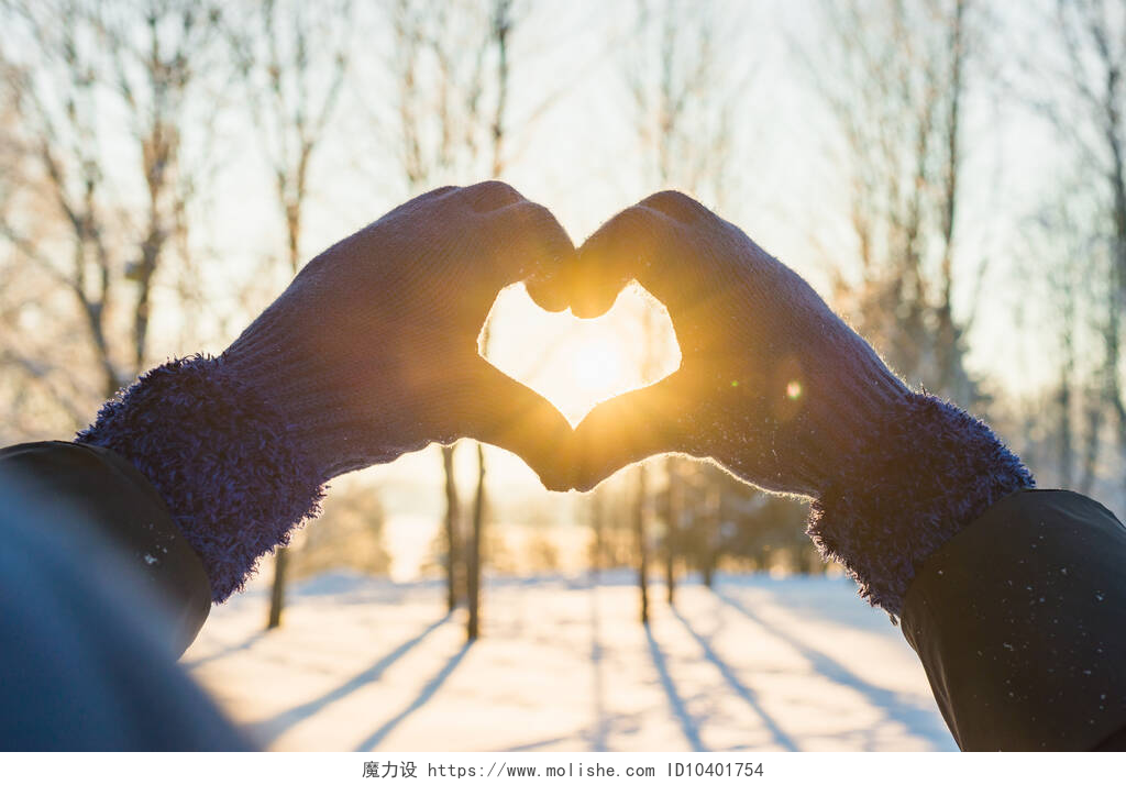 在冬天里比心的一双手手戴手套、冬夜明媚、太阳光、情人节、爱情观念的女人制造心形符号.